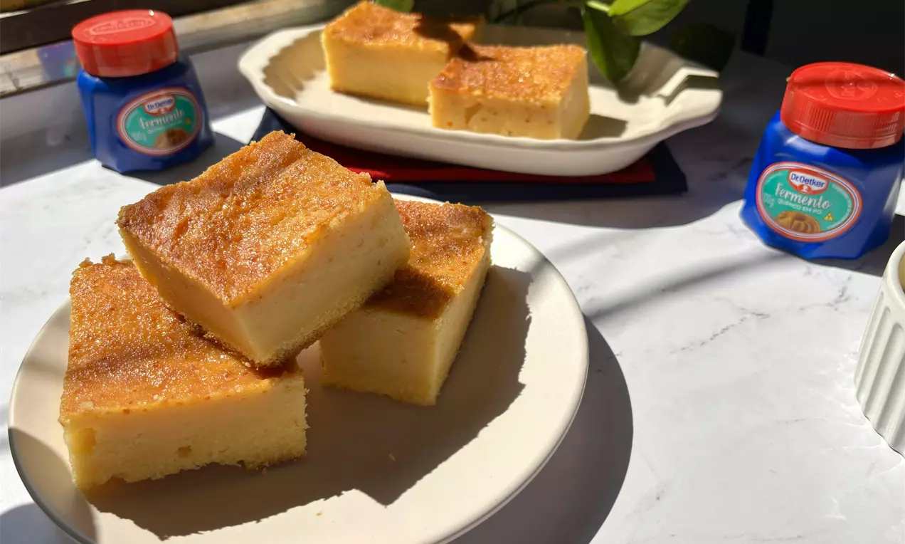 Fatias douradas de bolo de fubá cremoso, com textura macia e superfície levemente crocante, servidas em pratos brancos sobre mesa iluminada