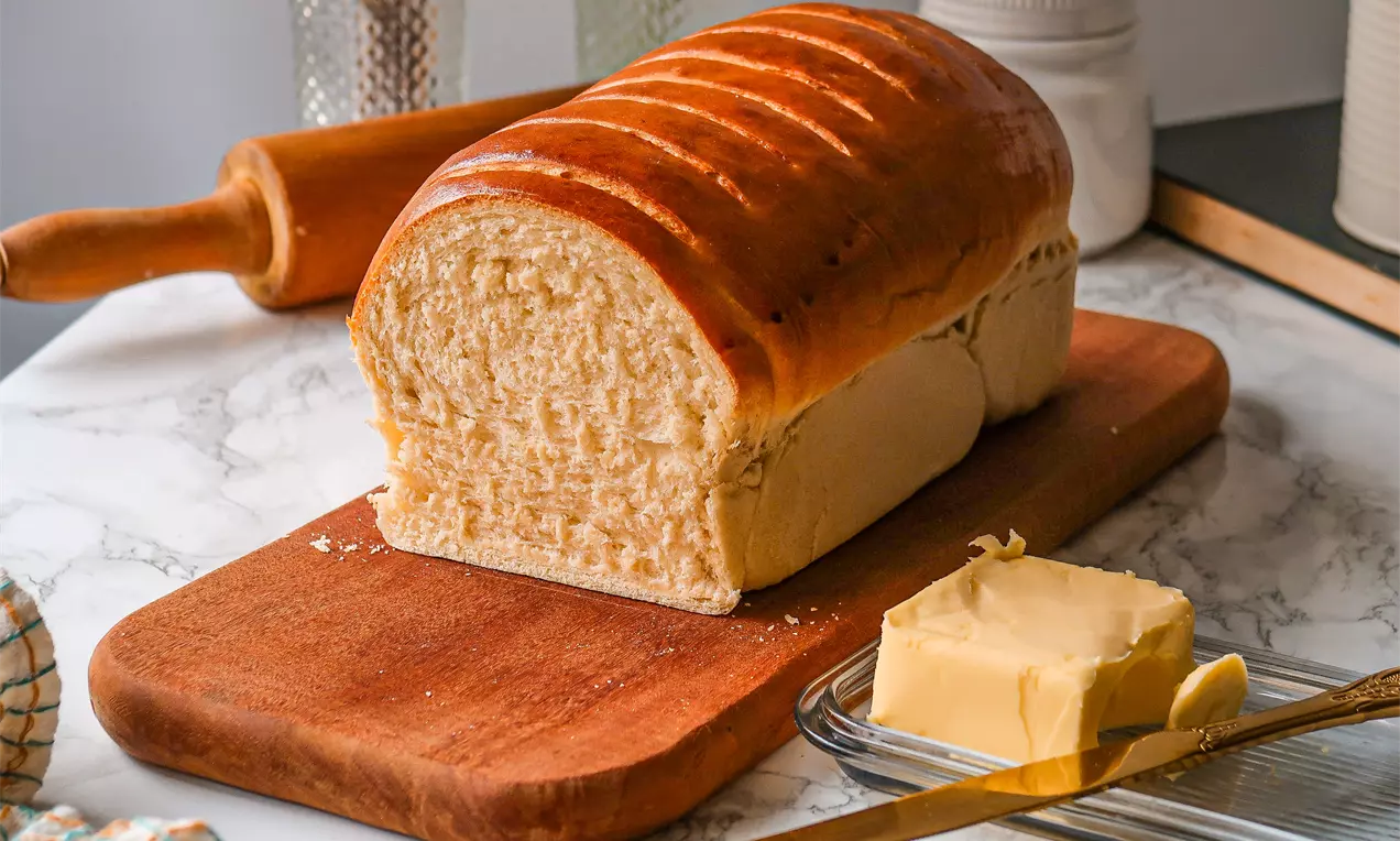 Pão caseiro super fofinho com crosta dourada e miolo branco e aerado, fatias com manteiga sobre tábua de madeira rústica