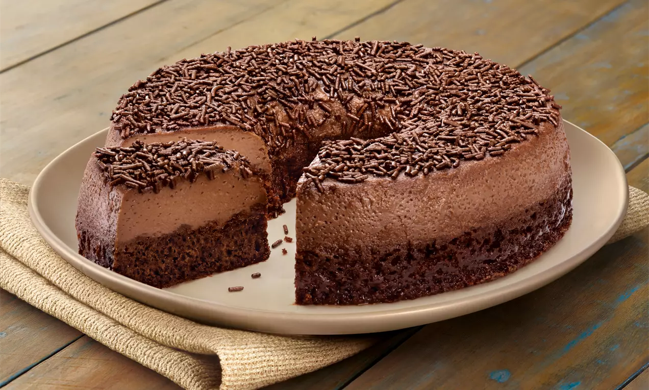Bolo Brigadeirão em forma de anel, com camada cremosa de chocolate, base densa, cobertura de granulado escuro em prato claro sobre tecido