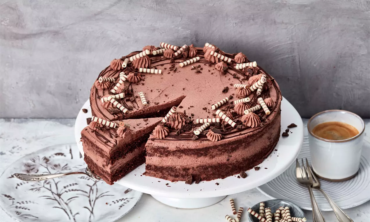 Bolo mousse de chocolate marrom escuro em camadas suaves, decorado com arabescos de chantilly e rolinhos de biscoito listrados sobre prato branco