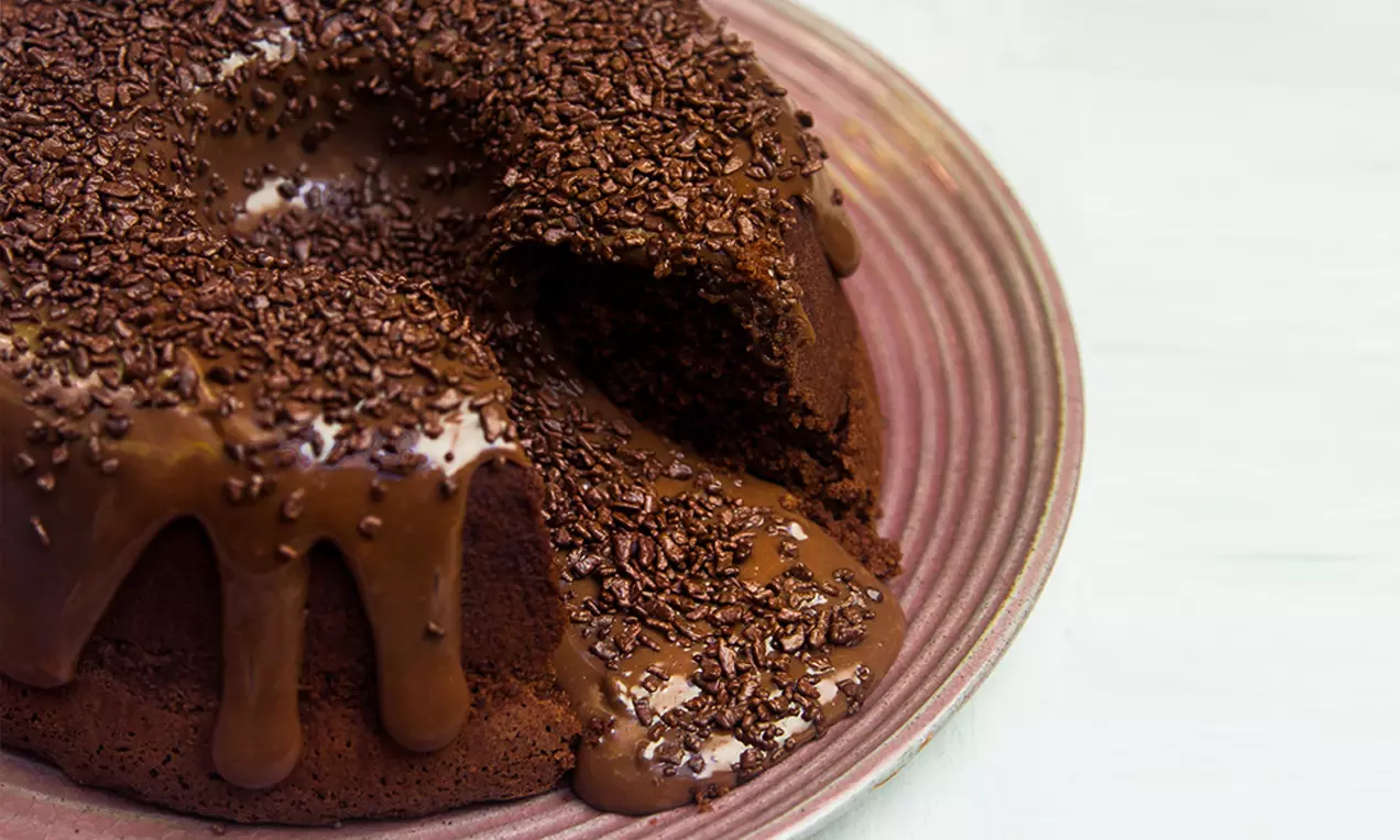 Bolo Vulcão de Chocolate com cobertura de ganache brilhante escorrendo pelo topo, fatia mostrando miolo úmido e raspas de chocolate