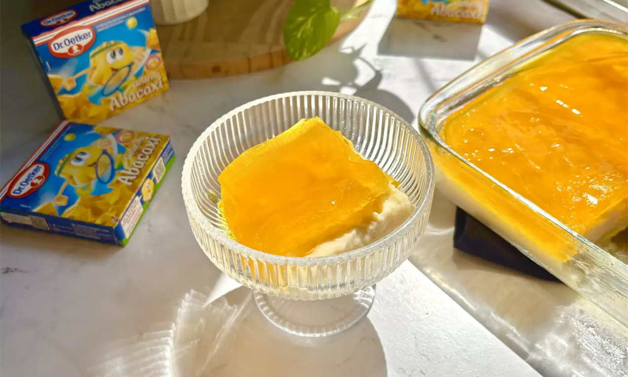 Fatias retangulares de gelado de abacaxi amarelo brilhante sobre base cremosa branca em taça transparente ao lado de uma travessa