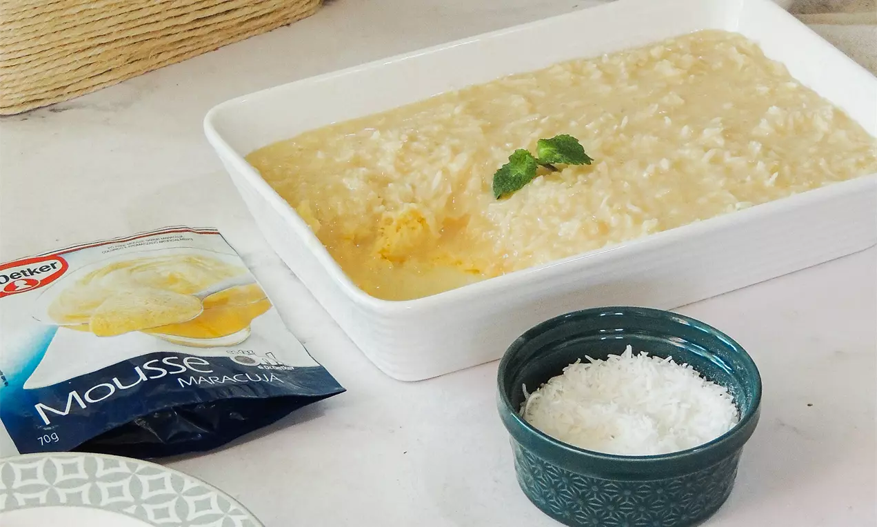 Mousse de maracujá amarelo-claro com cocada cremosa em travessa branca, decorada com folhas verdes e acompanhada de coco ralado em potinho