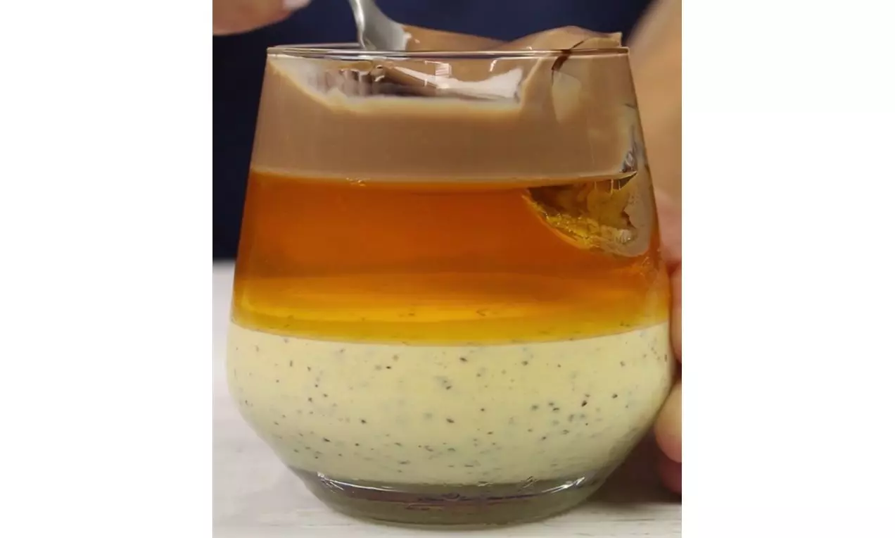 Camada superior de gelatina dourada e translúcida sobre creme amarelo claro com sementes de maracujá, servida em um copo transparente