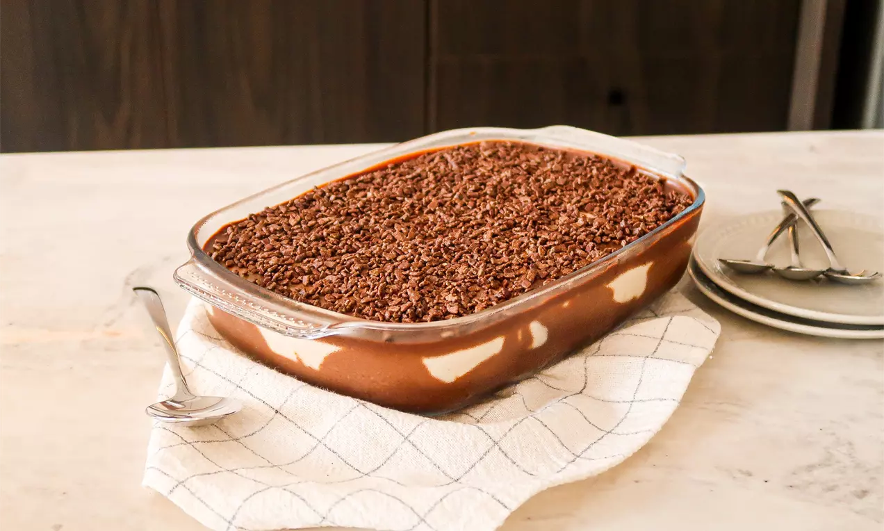 Mousse de maracujá trufado com creme amarelo em camadas dentro de um refratário transparente, coberto com raspas de chocolate marrom