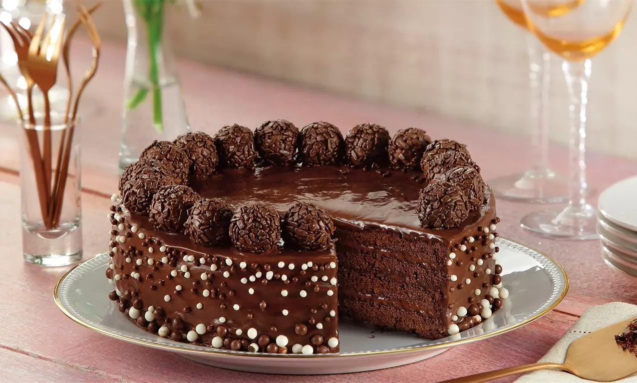 Bolo de aniversário de chocolate decorado com ganache brilhante, morangos frescos, confeitos coloridos e velas sobre prato branco
