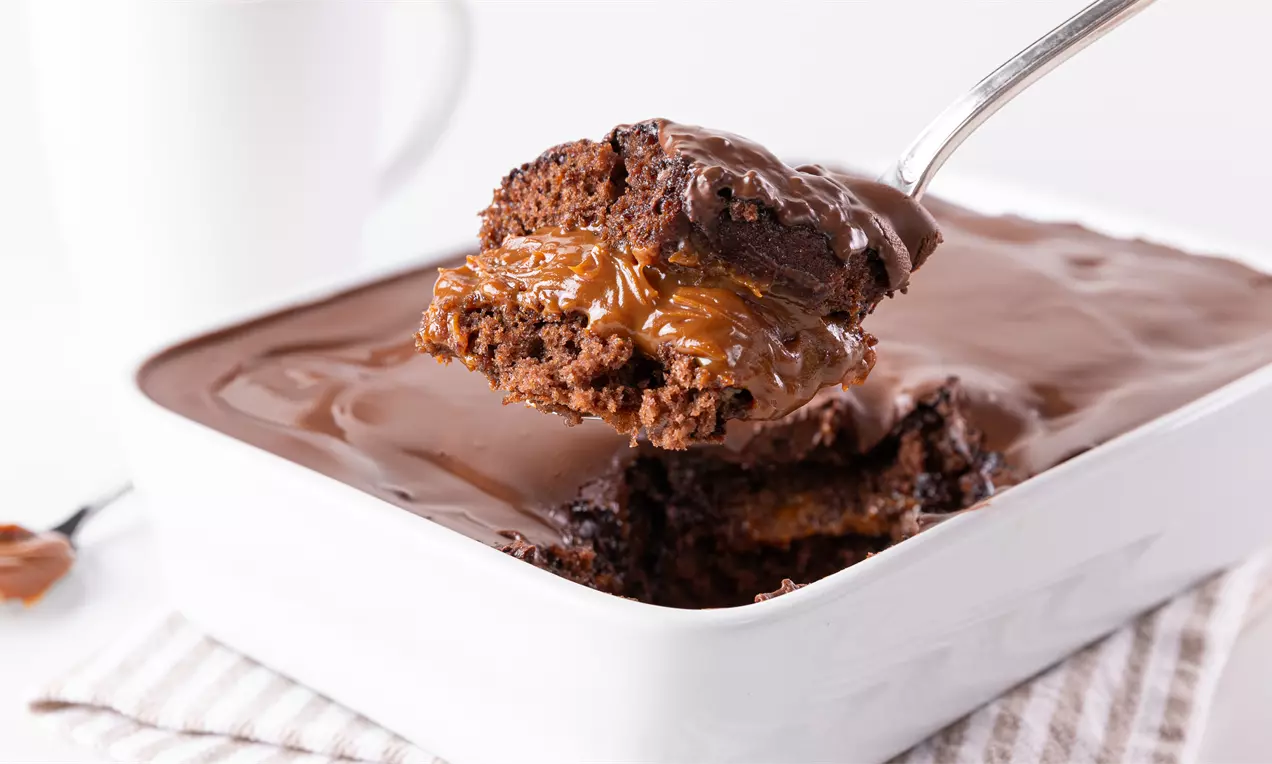 Pão de mel na travessa coberto por ganache de chocolate brilhante, fatias revelando recheio cremoso e polvilhado com cacau e nozes