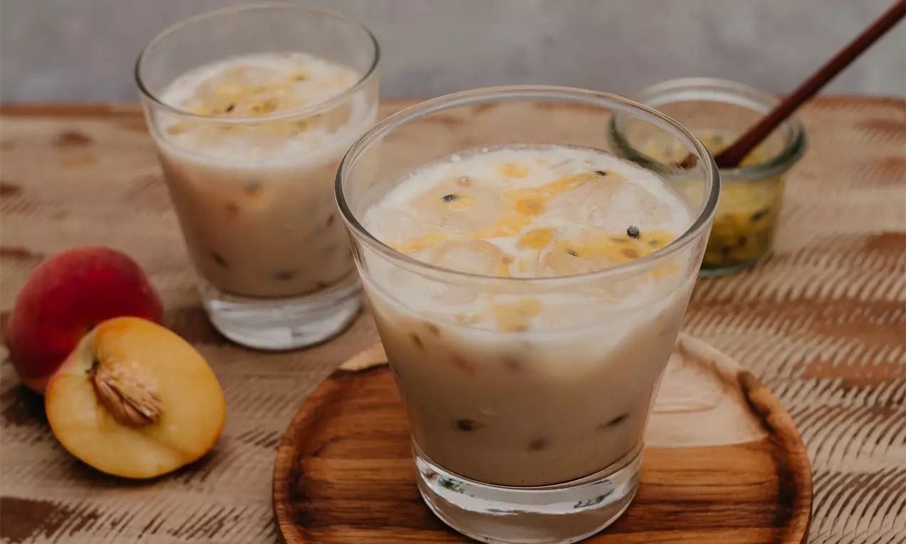 Gin de cor areia suave com pedaços pretos de maracujá distribuídos sobre a superfície cremosa em copo transparente sobre prato de madeira clara