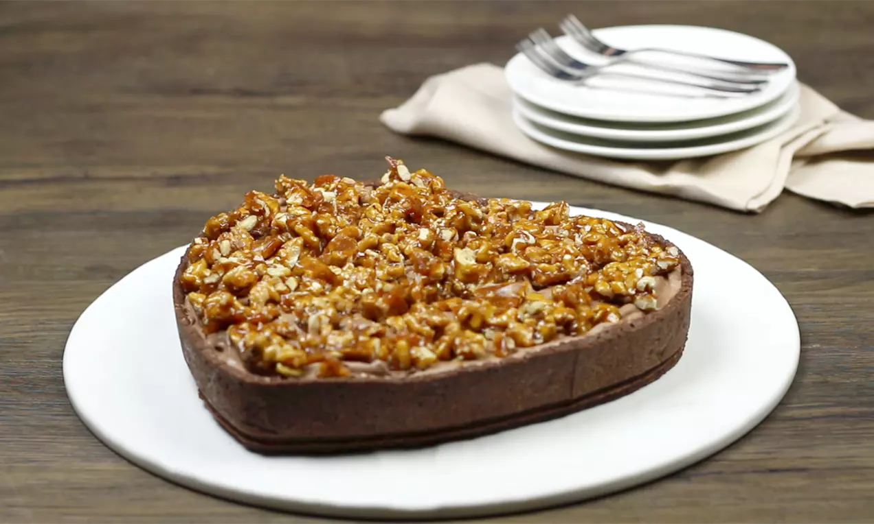Torta em forma de coração com borda de massa crocante escura, recheio de nozes caramelizadas brilhantes sobre prato branco redondo