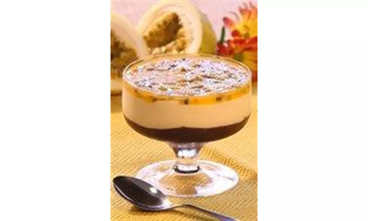 Mousse de maracujá creme amarelo pálido sobre camada escura de chocolate em taça de vidro com calda brilhante e sementes sobre toalha amarela